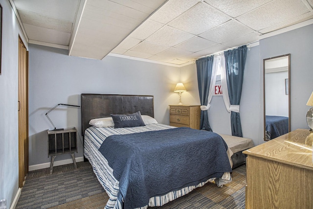 bedroom with dark colored carpet, a paneled ceiling, and baseboards