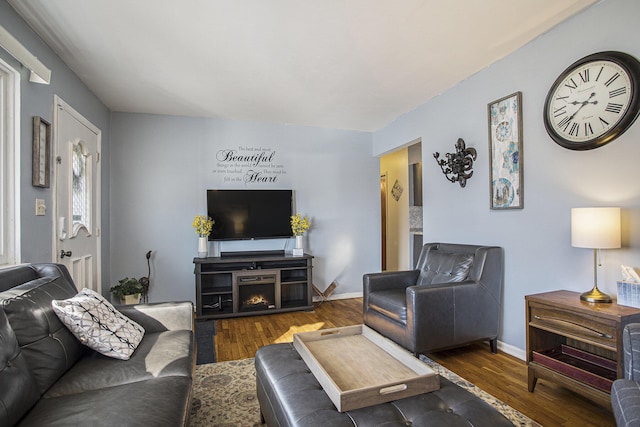 living area with a lit fireplace, wood finished floors, and baseboards