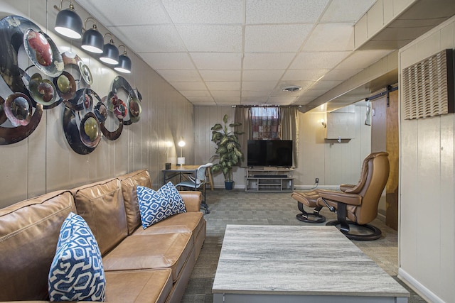 living room featuring a paneled ceiling, visible vents, dark carpet, wood walls, and baseboards