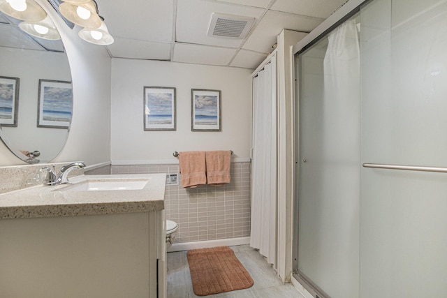 bathroom with tile walls, a paneled ceiling, visible vents, wainscoting, and vanity