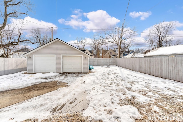 snow covered garage featuring a garage and fence