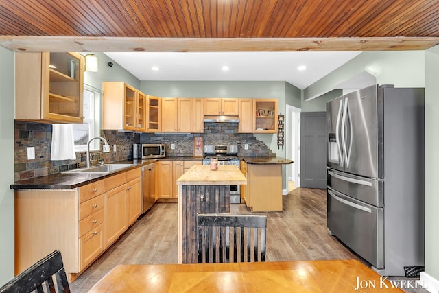 kitchen with glass insert cabinets, a center island, stainless steel appliances, light brown cabinetry, and a sink