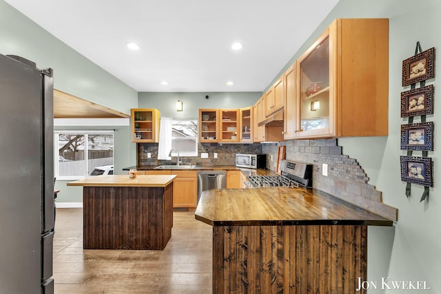 kitchen with wooden counters, appliances with stainless steel finishes, glass insert cabinets, and under cabinet range hood