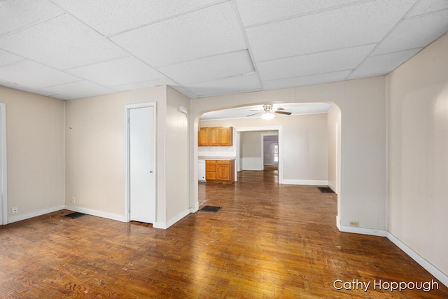 unfurnished room featuring arched walkways, a drop ceiling, and wood finished floors