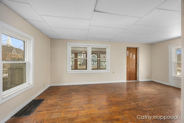 unfurnished room featuring baseboards, visible vents, a drop ceiling, and wood finished floors