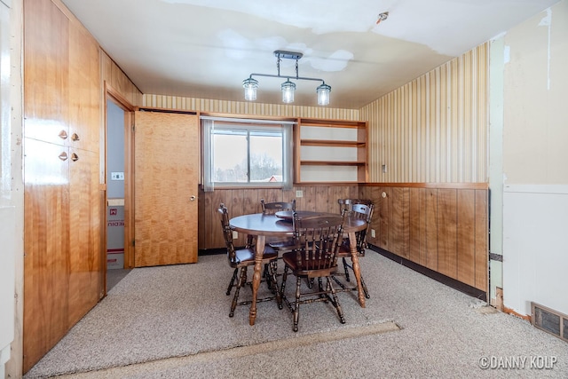 carpeted dining space featuring wood walls, visible vents, and a wainscoted wall