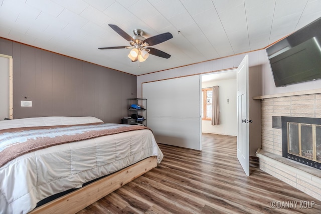 bedroom with a fireplace, a ceiling fan, and wood finished floors