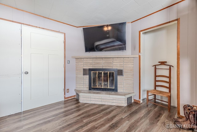 living room with a brick fireplace, ornamental molding, and wood finished floors