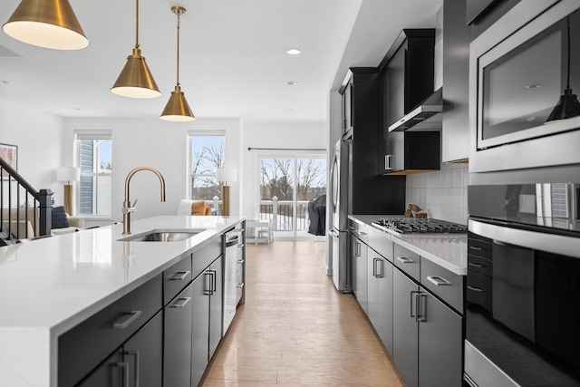 kitchen with an island with sink, hanging light fixtures, stainless steel appliances, light countertops, and a sink