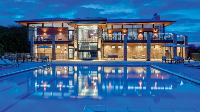 pool at dusk featuring a patio area, fence, and a community pool