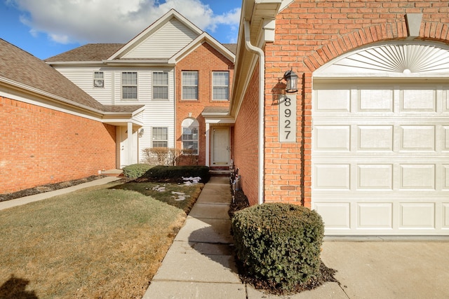 property entrance featuring a garage, brick siding, and a lawn