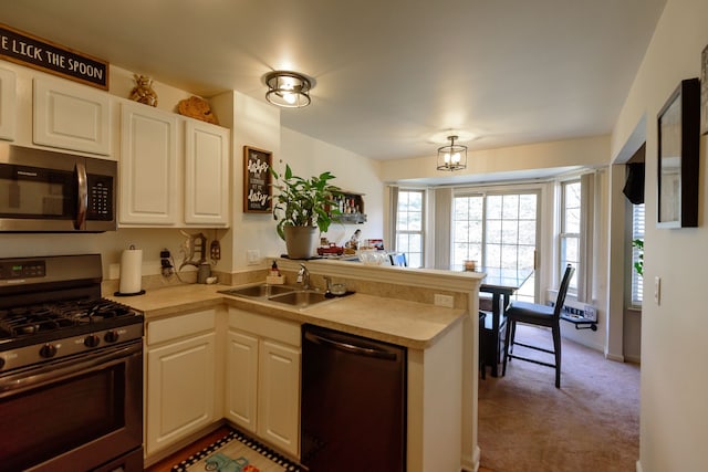 kitchen with white cabinets, a peninsula, stainless steel appliances, light countertops, and a sink