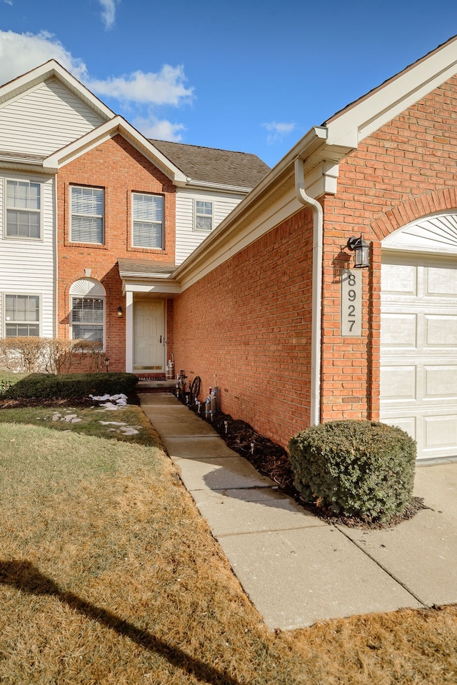 doorway to property featuring a yard, brick siding, and an attached garage