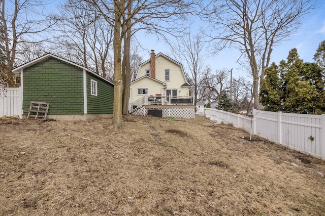 back of property with a chimney, a gambrel roof, a wooden deck, and a fenced backyard