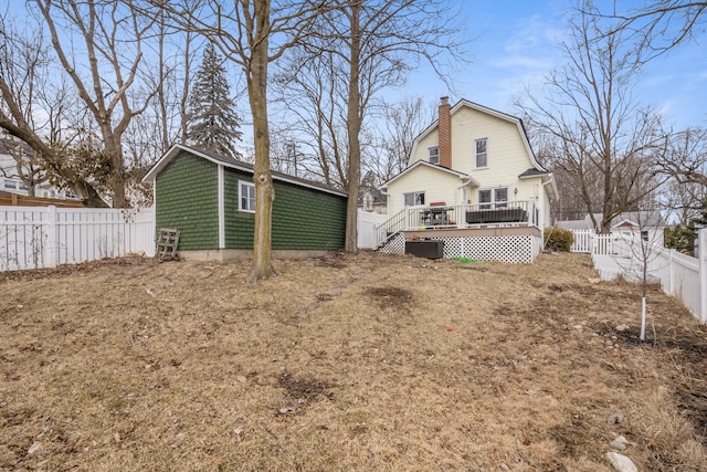 back of house featuring a gambrel roof, a chimney, a deck, a fenced backyard, and an outbuilding