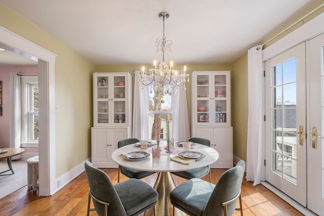 dining space featuring light wood finished floors, a chandelier, french doors, and baseboards