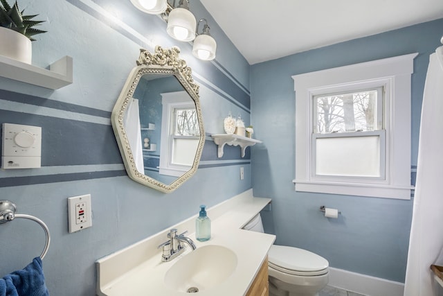 bathroom featuring baseboards, plenty of natural light, toilet, and vanity