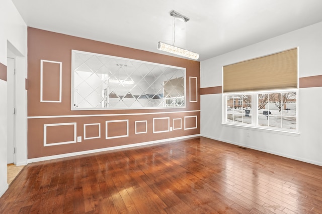 empty room featuring wood-type flooring, visible vents, and baseboards