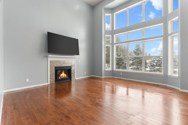 35316 Burgundy, Sterling Heights, MI 48312 - unfurnished living room featuring hardwood / wood-style floors, a glass covered fireplace, a towering ceiling, and baseboards