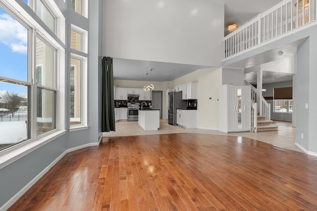 35316 Burgundy, Sterling Heights, MI 48312 - unfurnished living room with stairs, a high ceiling, light wood-style flooring, and baseboards
