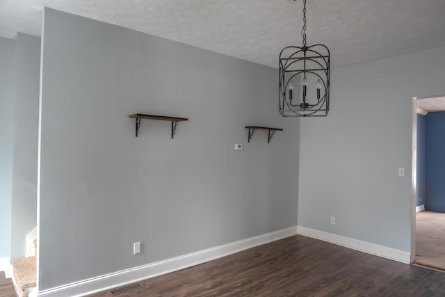 unfurnished dining area featuring baseboards, visible vents, dark wood-style flooring, an inviting chandelier, and a textured ceiling