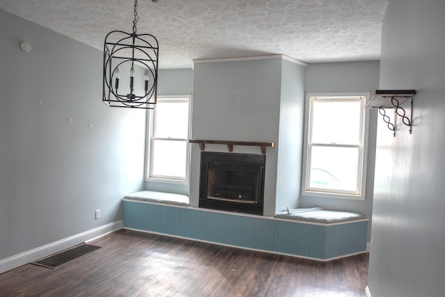 unfurnished living room with a notable chandelier, dark wood-style flooring, a fireplace, visible vents, and baseboards