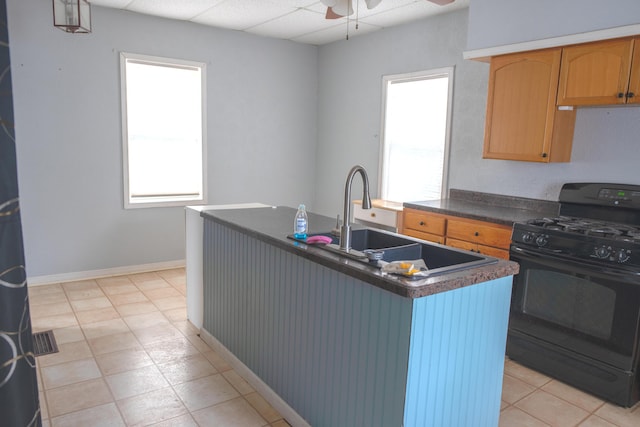 kitchen with black gas range, dark countertops, a kitchen island with sink, a paneled ceiling, and a sink