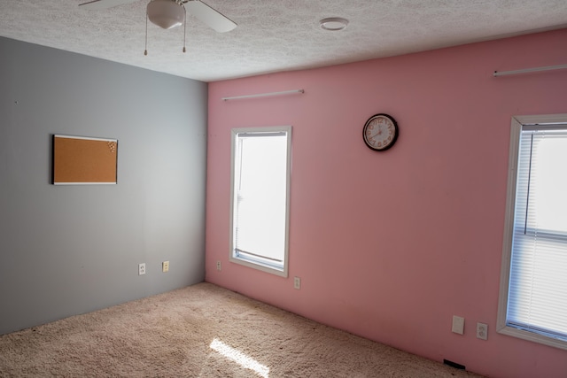 unfurnished room with a healthy amount of sunlight, ceiling fan, carpet floors, and a textured ceiling