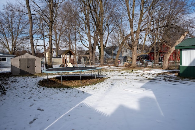 yard covered in snow with a trampoline, an outbuilding, playground community, and a storage unit