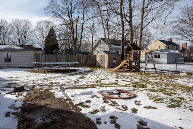 yard layered in snow featuring an outbuilding, a playground, fence, a storage unit, and a trampoline