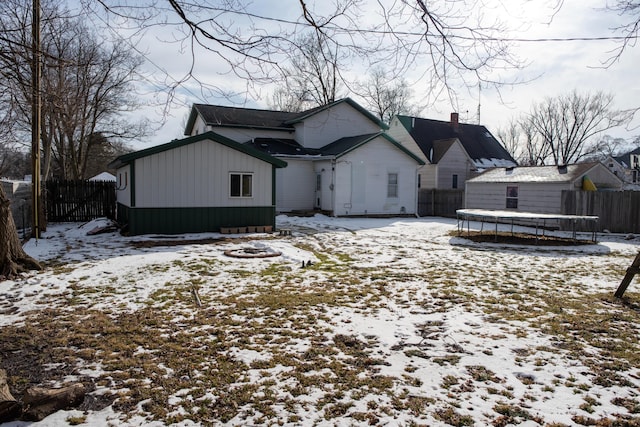 snow covered back of property with a trampoline and fence