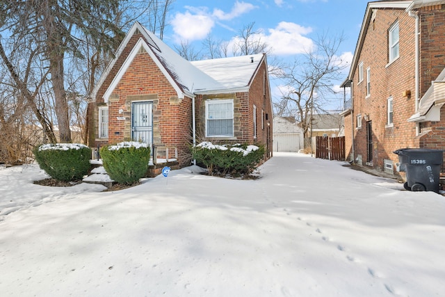 view of snowy exterior featuring a garage, brick siding, and fence