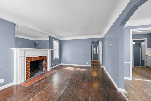 unfurnished living room with arched walkways, hardwood / wood-style floors, a brick fireplace, and baseboards