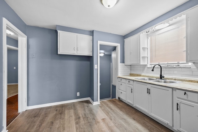 kitchen with decorative backsplash, light wood-style flooring, light countertops, white cabinetry, and a sink