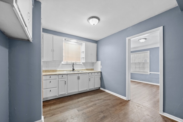 kitchen with tasteful backsplash, light countertops, light wood-type flooring, white cabinetry, and a sink