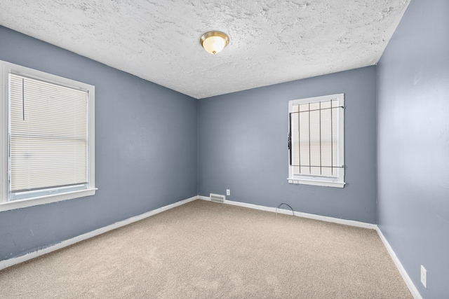 unfurnished room featuring carpet floors, baseboards, visible vents, and a textured ceiling