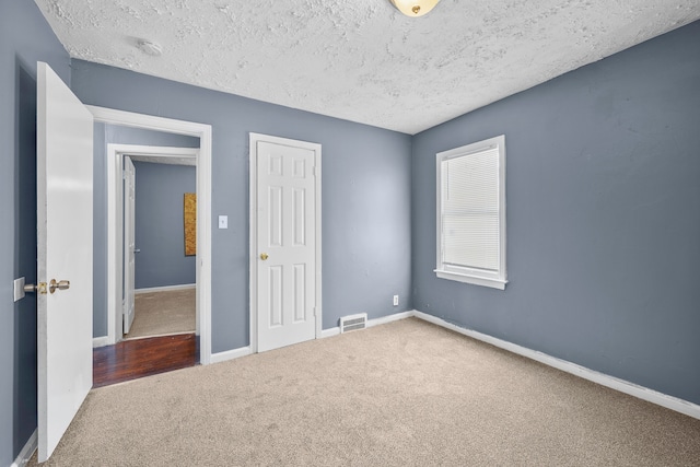 carpeted spare room featuring a textured ceiling, visible vents, and baseboards