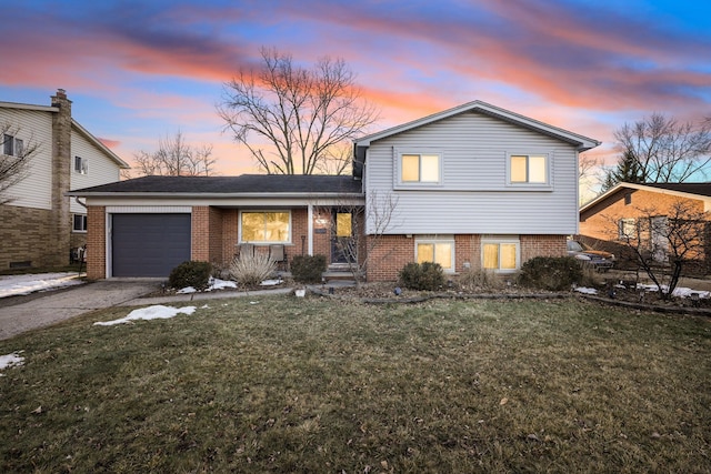 tri-level home with an attached garage, aphalt driveway, a lawn, and brick siding