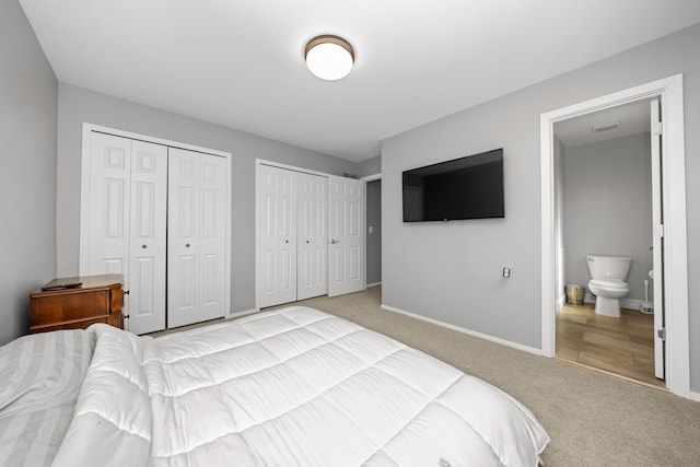 bedroom with ensuite bathroom, carpet flooring, visible vents, baseboards, and multiple closets