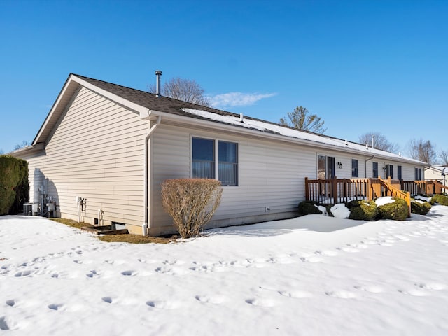 snow covered rear of property with a deck and central AC unit