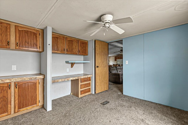 kitchen with brown cabinets, built in desk, light countertops, a ceiling fan, and carpet flooring