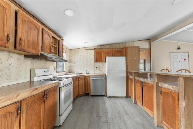 kitchen featuring white appliances, under cabinet range hood, brown cabinetry, and wallpapered walls