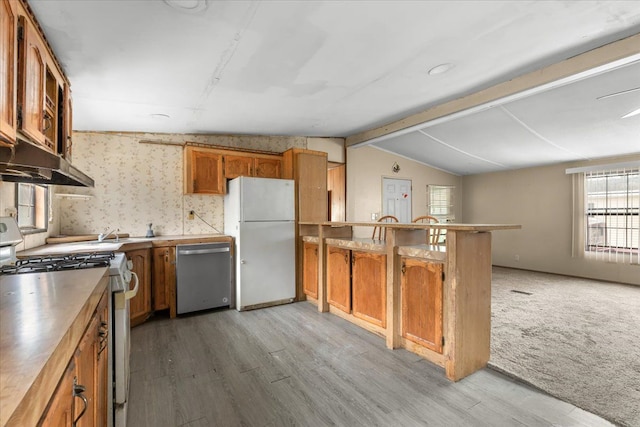 kitchen featuring white appliances, brown cabinetry, vaulted ceiling with beams, a peninsula, and under cabinet range hood