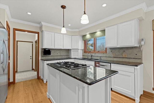 kitchen featuring light wood finished floors, crown molding, appliances with stainless steel finishes, white cabinets, and a sink