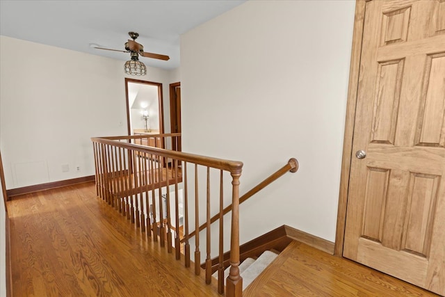 hallway with an upstairs landing, baseboards, and light wood-style floors
