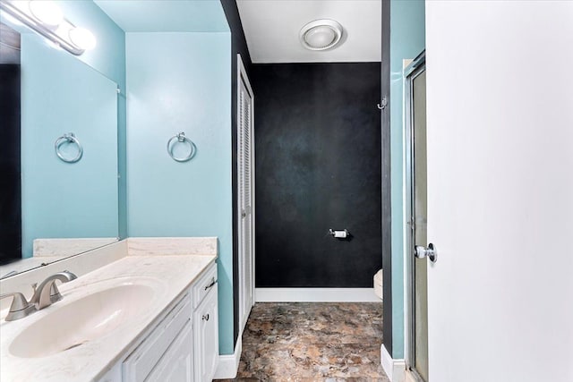 bathroom featuring baseboards, toilet, stone finish floor, a shower with shower door, and vanity