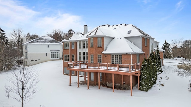 snow covered back of property with a deck and brick siding