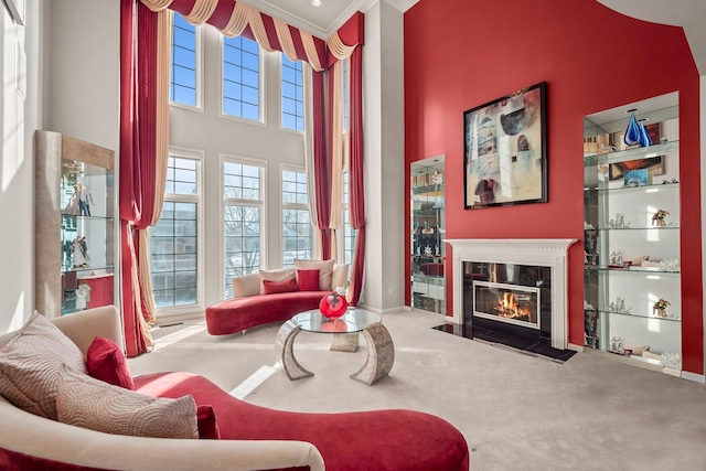 living area featuring carpet floors, a high ceiling, crown molding, and a glass covered fireplace