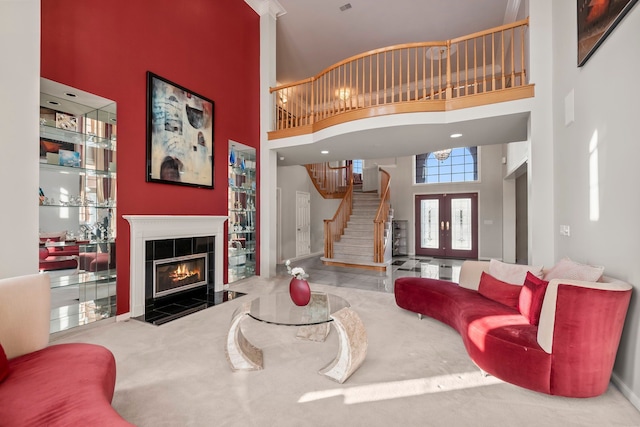 living area with stairs, french doors, a tiled fireplace, and a towering ceiling