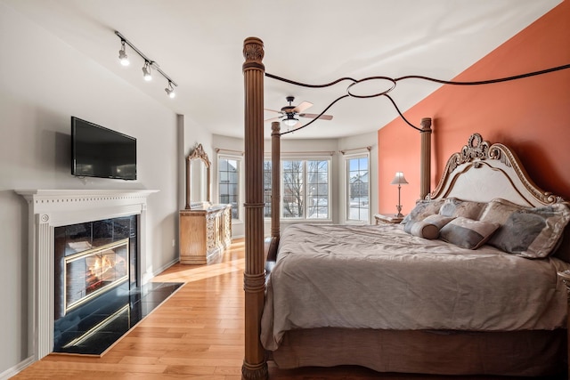 bedroom featuring baseboards, a fireplace, track lighting, and wood finished floors